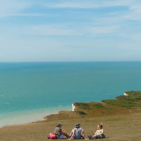Friends picnicking on a clifftop above turquoise water — Seven Sisters